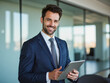 © f_bossa - A portrait headshot photo of a professional CEO executive business worker: A man in a blue suit is smiling and holding a tablet