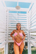 © svetograph - A woman in a bikini stands in front of a white shower stall. She is smiling and she is enjoying the moment
