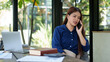 © Pichsakul - Businesswoman talking on phone while working on laptop in a natural-themed workspace with greenery and glass windows