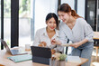 © David - Two smiling happy asian businesswomen working together on a laptop in the office, demonstrating teamwork business meeting in a corporate and collaboration