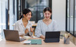 © David - Happy professional young women collaborating with enthusiasm in a modern office setting. Two asian female entrepreneurs using a laptop for a productive business meeting in a corporate workplace.