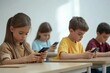 © Vision Clarity - Focused schoolchildren using cellphones while sitting at desks in school classroom interior during break, copy space