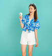 © sitthiphong - Full body length happy smiling young Asian woman in summer wearing floral shirt holding fan to cool herself with suffers from too hot weather in blue background.