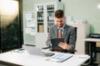 © Nuttapong punna - Confident businessman working on finance analysis with a tablet and laptop at office desk