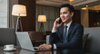 © Bagas - Smiling Businessman Using Laptop and Phone in Hotel Lobby