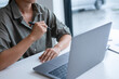 © MIND AND I - Businesswoman sitting at desk on couch in workplace or at home working on laptop and analyzing data on charts and graphs and writing on papers to make business plan and strategies for company,