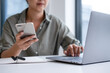 © MIND AND I - Businesswoman sitting at desk on couch in workplace or at home working on laptop and analyzing data on charts and graphs and writing on papers to make business plan and strategies for company,