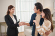 © eggeeggjiew - Young Asian couple receives keys from female real estate agent and shakes hands while standing happily in their new living room.