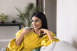 © fizkes - Indian woman relaxing on sofa holds smartphone leaves audio message, sending voicemail to friend, lead remote talk through speakerphone, using virtual assistant. Digital communication, modern AI tech