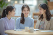 © S.Jirut - Close-Up of Three Confident Young Office Ladies in Candid Conversation Around Polished Light Oak Meeting Table with Steaming Coffee and Cozy Office Background