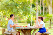 © Marcio - Mother and adult son enjoying a relaxing coffee break at a wooden picnic table in a green park.  Concept of family love, bonding and Mother's Day