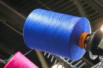 Poster - A blue spool of thread is hanging from a rack. The spool is made of a synthetic material and is about the size of a tennis ball. It is hanging from a metal rack that is attached to the ceiling
