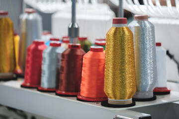 Poster - A row of colorful spools of thread are displayed on a table. The spools are of various colors and sizes, and they are arranged in a neat and orderly fashion. Concept of creativity and craftsmanship
