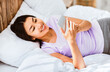 © Prostock-studio - Smiling Asian Girl With Smartphone Using Mobile App Lying In Bed At Home On Weekend Morning. High-Angle Shot