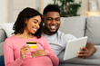 © Prostock-studio - Closeup of happy african expecting couple making shopping online from home, using digital tablet and credit card, free space
