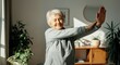 © Artyom - Elderly woman doing morning yoga indoors, stretching arms, enjoying sunlight