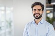 © PlanetOfVectors - Confident smiling man with curly hair and beard wearing a blue shirt, standing in a modern office background with blurred lights and plants. Ai generative