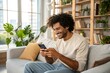 © NISHAN'S STUDIO - Happy Young Man Using Smartphone on Cozy Couch in Stylish Living Room