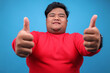 © Gatot - Young Big Guy Wear Red Clothes Smiling And Showing Thumbs Up On Blue Studio Wall