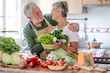 © luciano - Attractive senior couple working together in home kitchen preparing vegetables. Caucasian elderly smiling people retirees enjoying healthy eating