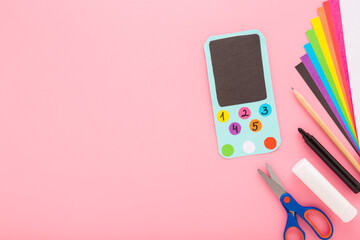 Wall Mural - Smartphone, glue, scissors, marker, pencil and colorful application paper on light pink table background. Pastel color. Creating child gadget for playing. Closeup. Empty place for text. Top down view.