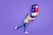 © deagreez - Cheerful elderly woman holding multi-colored balloons on a vibrant purple background