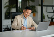 © Anna - Smiling Asian middle-aged man working on documents at modern office desk