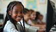 © miss irine - Young afro girl smiles using computer in classroom. Student studies on PC, surfs internet, researches datum, lessons. Happy child uses tech in education, browses network. High childhood cognition.