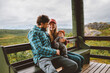 © EVERST - Family lifestyle father and mother with infant baby sitting on terrace traveling in Norway, parents with child happy candid emotions bonding together