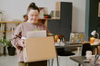 © AnnaStills - Wide shot of young woman with down syndrome carrying cardboard box with houseplant and notebooks in modern office
