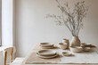 © kollibri - A beautifully arranged dining table featuring simple ceramic dishes, a neutral tablecloth, and a vase with dried flowers, creating a calming ambiance