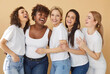 © Studio Romantic - Group portrait of diverse women in casual white t shirts gather together and have fun, laugh at something funny, feel overjoyed, isolated over beige studio background. Diversity concept