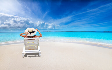 Wall Mural - a holiday woman with a sunhat sits on a lounge chair at a tropical paradise beach with turquoise oce