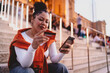 © BullRun - stylish young woman sits on outdoor steps, focused on making an online payment. Female holds credit card in one hand and smartphone in the other, enjoying digital shopping in a vibrant urban setting