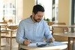 © New Africa - Handsome business owner doing paperwork at table in his cafe