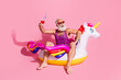 © deagreez - Elderly man in cheerful attire enjoying a fun summer day on a unicorn float with a drink in hand