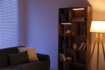 Poster - stylish living room with comfortable sofa and wooden shelving unit in evening. interior design