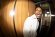 © Jimena Roquero/Stocksy - Portrait in elevator of young man smiling. Fisheye