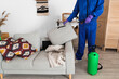 © Pixel-Shot - Male worker disinfecting sofa in room