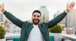 © Postmodern Studio - Young hispanic male joyously celebrating on rooftop with cityscape background