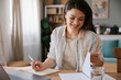 © Mihajlo Ckovric/Stocksy - Focused Woman Writing Notes While Working on a Laptop at Home