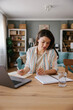 © Mihajlo Ckovric/Stocksy - Focused Woman Writing Notes While Working on a Laptop at Home