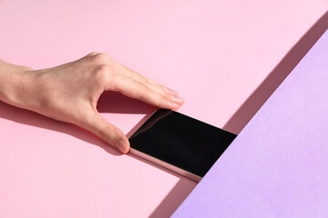 Wall Mural - female hand hiding mobile phone under purple layer on pink background