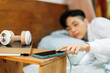 © Jimena Roquero/Stocksy - Young woman in cozy bedroom stopping phone alarm from bed