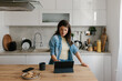 © Mihajlo Ckovric/Stocksy - Young Woman Using Tablet in Modern Kitchen While Relaxing With Coffee