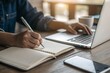 © khopidd232 - Person taking notes in notebook while using laptop for online learning and working remotely