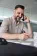 © Jovo Jovanovic/Stocksy - Man talking on mobile phone at the desk