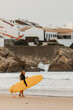 © Cavan Images - A female surfer with a yellow surfboard walks along the shore i