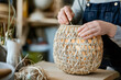 © Татьяна Евдокимова - Hands skillfully assembling a hand woven lampshade using natural fibers, showcasing traditional craftsmanship in a cozy workshop setting