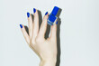 © Colour Laboratory/Stocksy - Hand with royal blue manicure holding beauty product nail polish